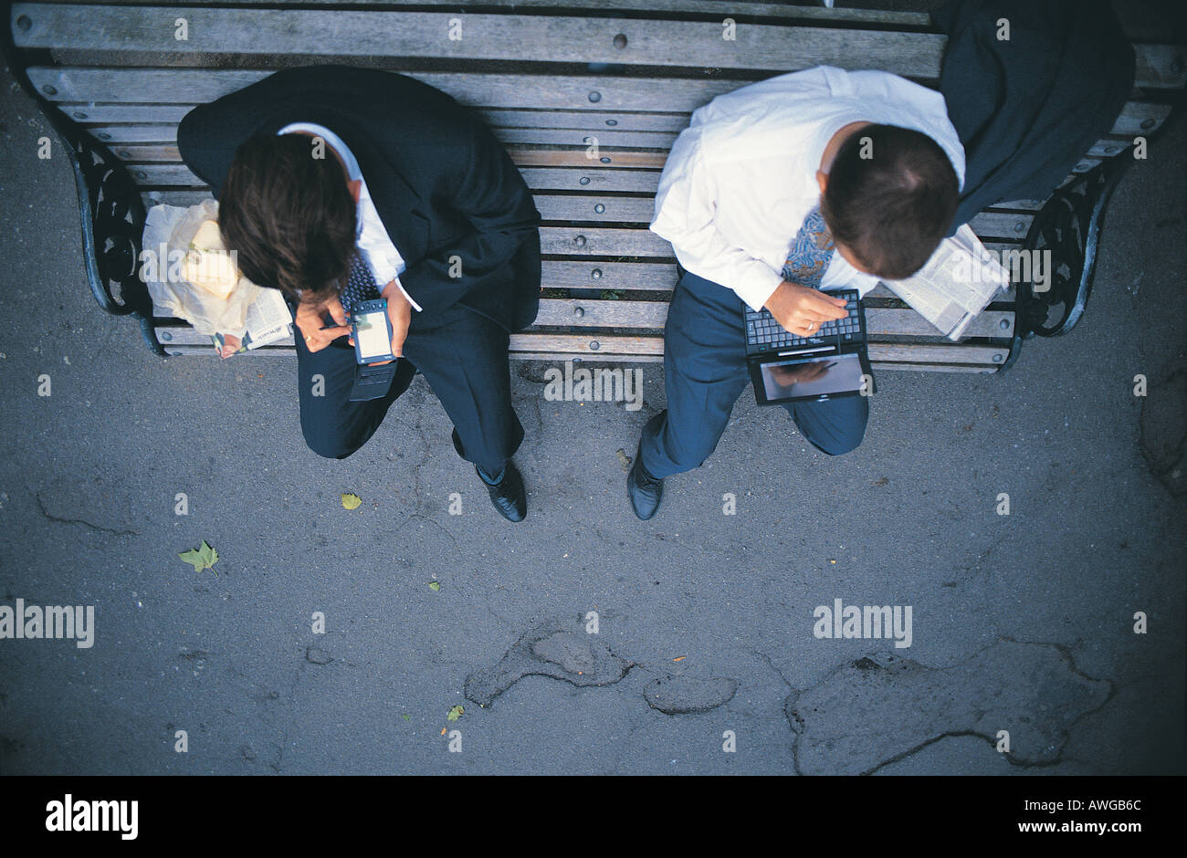 Two business men sitting on a bench using a palm and laptop having lunch Stock Photo