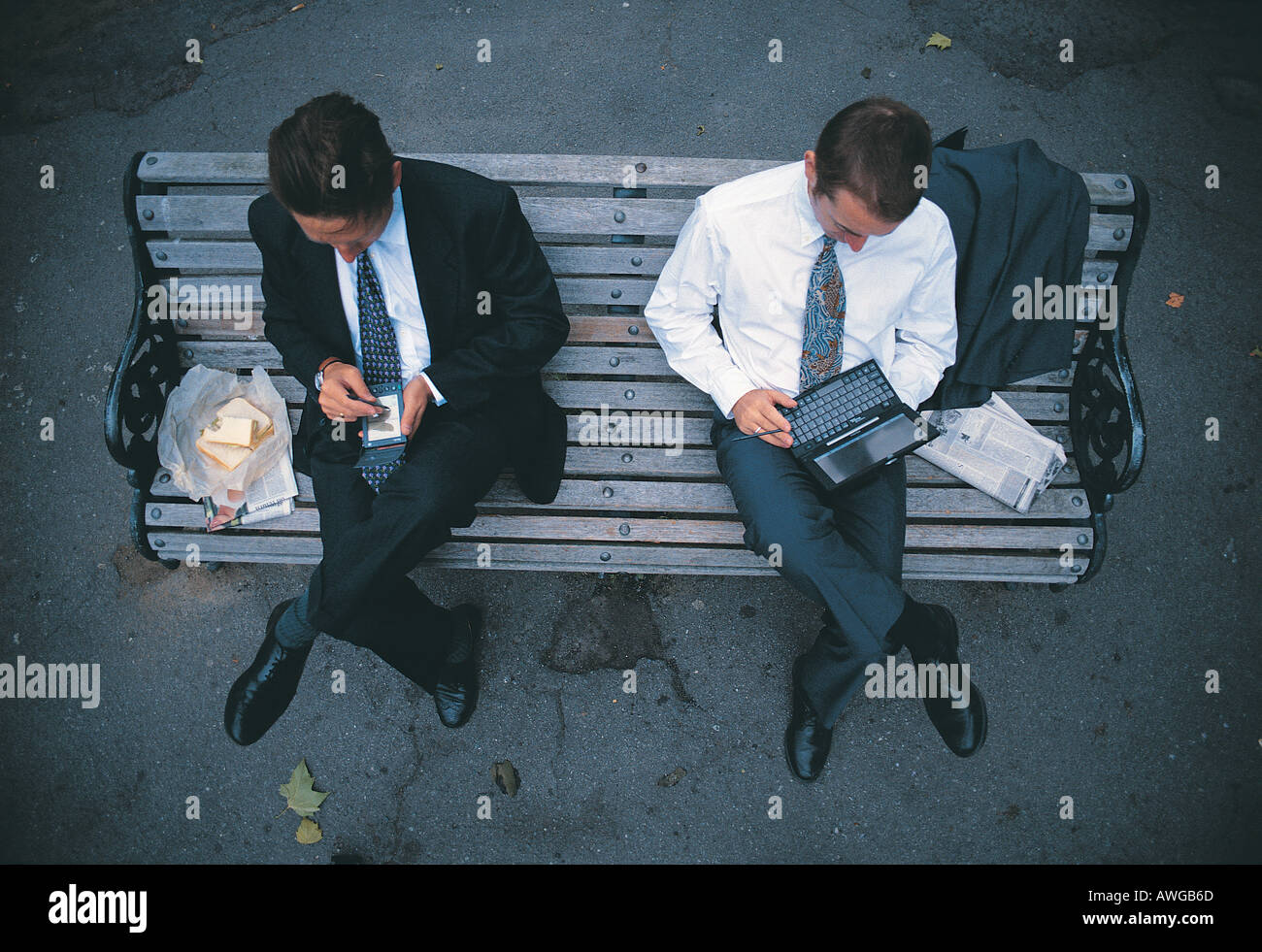 Two business men sitting on a bench using a palm and laptop having lunch Stock Photo
