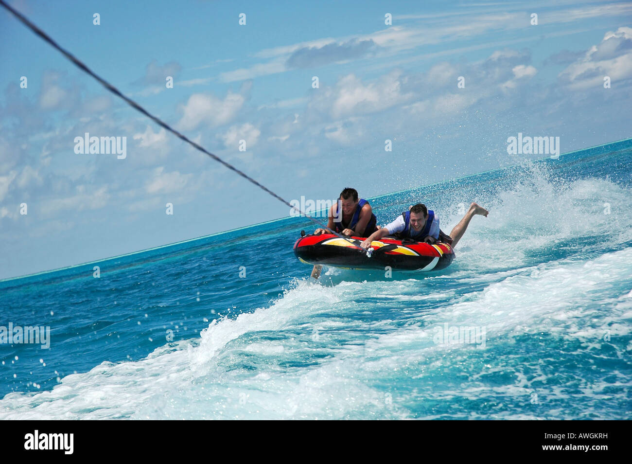 Horizontal close up of two young men riding an inflatable donut "tubing" as  it's being towed over the sea on a bright sunny day Stock Photo - Alamy