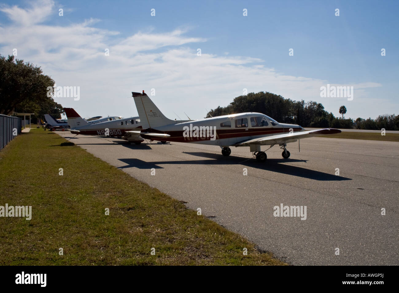 Line of small planes by the runway on a sunny day with wispy clouds in the sky Stock Photo