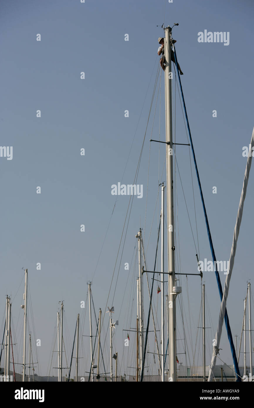 A man works at the top of the mast of his sailboat making repairs and