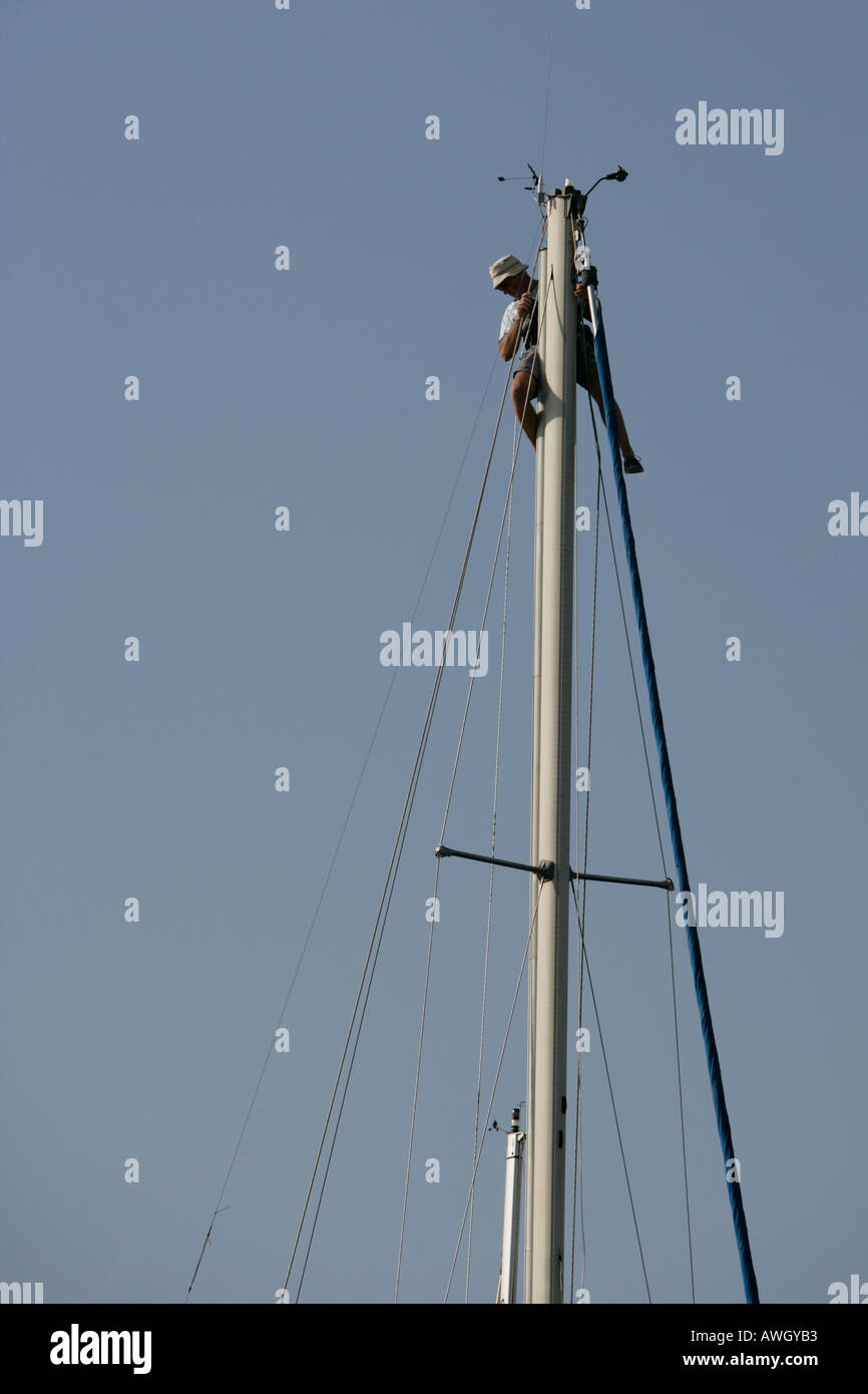 A man works at the top of the mast of his sailboat making repairs and