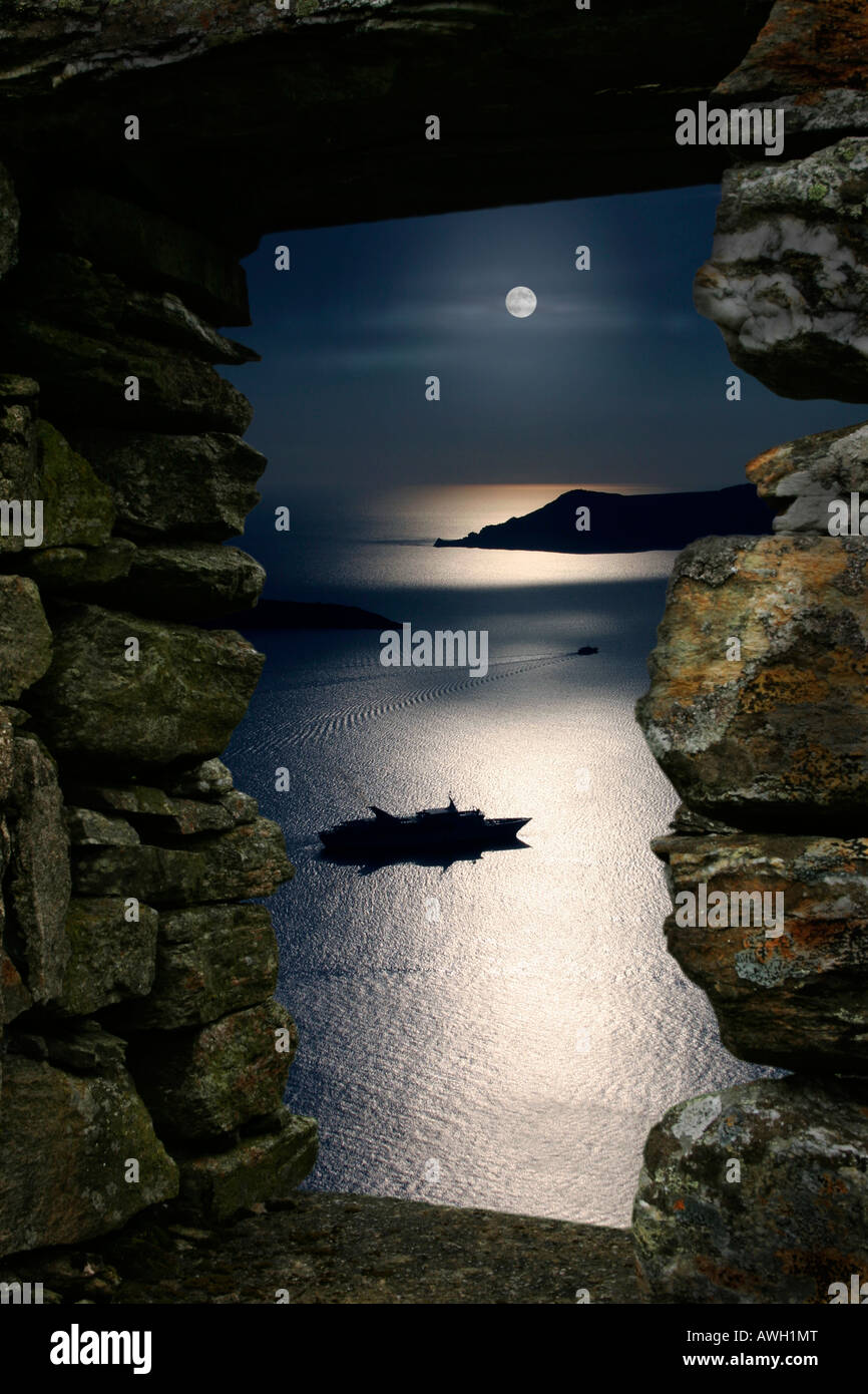 A ship at sea viewed through an old stone wall window by moonlight. Stock Photo
