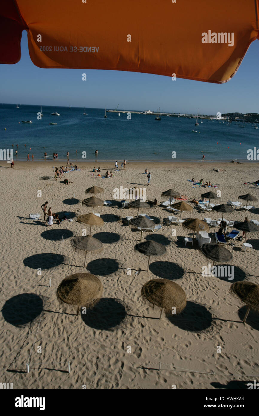 Thatched umbrellas make pools of shade on the beach named Praia da Rainha in the city of Cascais Portugal Stock Photo