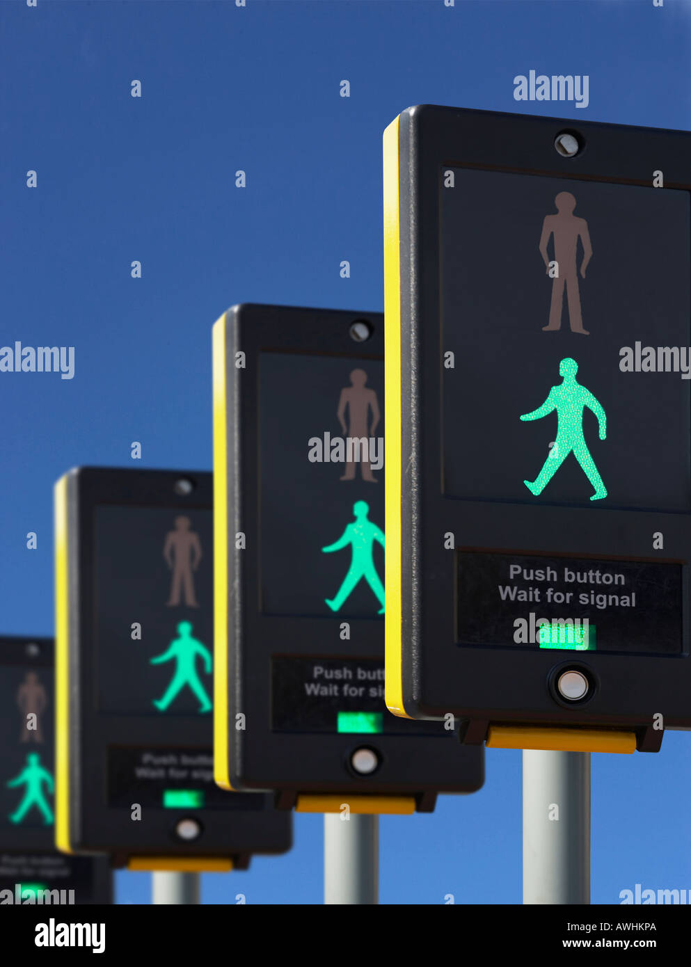 ROW OF FOUR PEDESTRIAN CROSSING CONTROL BOXES WITH ICON OF GREEN MAN ON BLUE SKY Stock Photo