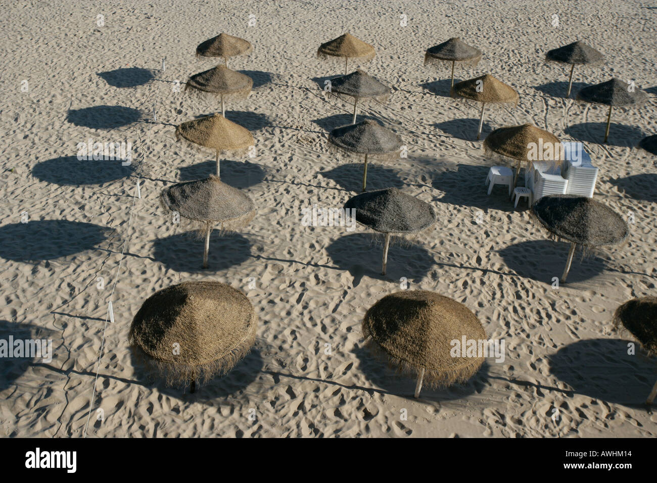 Thatched umbrellas make pools of shade on the beach named Praia da Rainha in the city of Cascais Portugal. Stock Photo