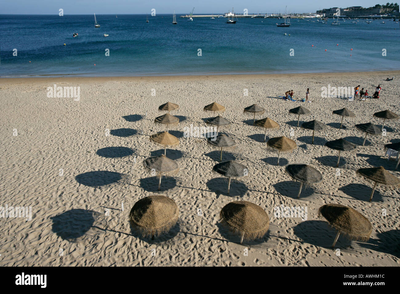 Thatched umbrellas make pools of shade on the beach named Praia da Rainha in the city of Cascais Portugal Stock Photo