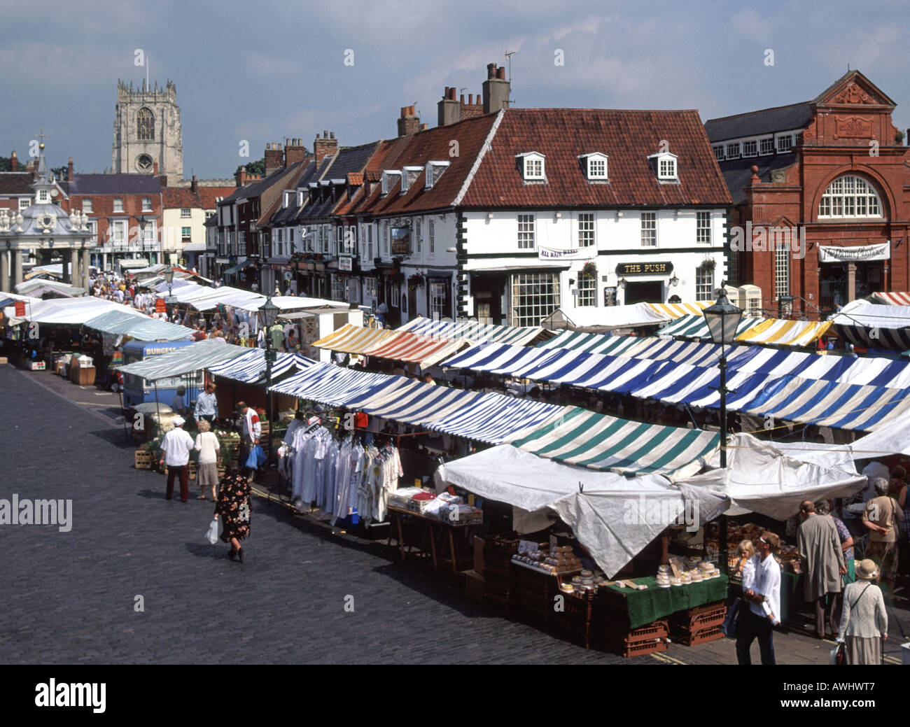 Looking down at people in market place with stalls & canopies historic market cross & church tower Beverley market town East Yorkshire England UK Stock Photo