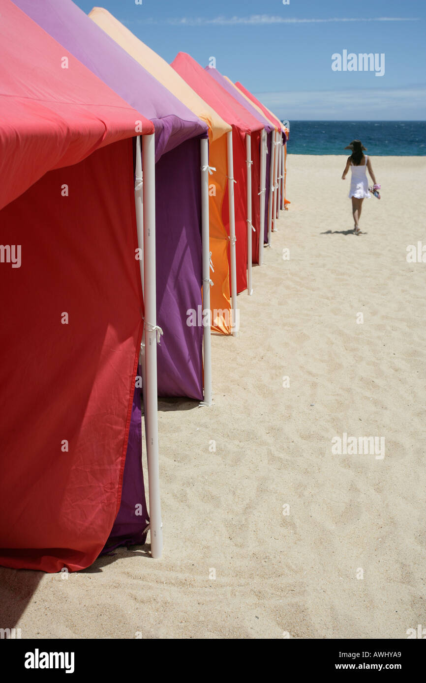 A woman walk past seasonal cabanas on the wide beaches at the coastal resort town of Nazaré on Portugal s Atlantic seaboard Stock Photo