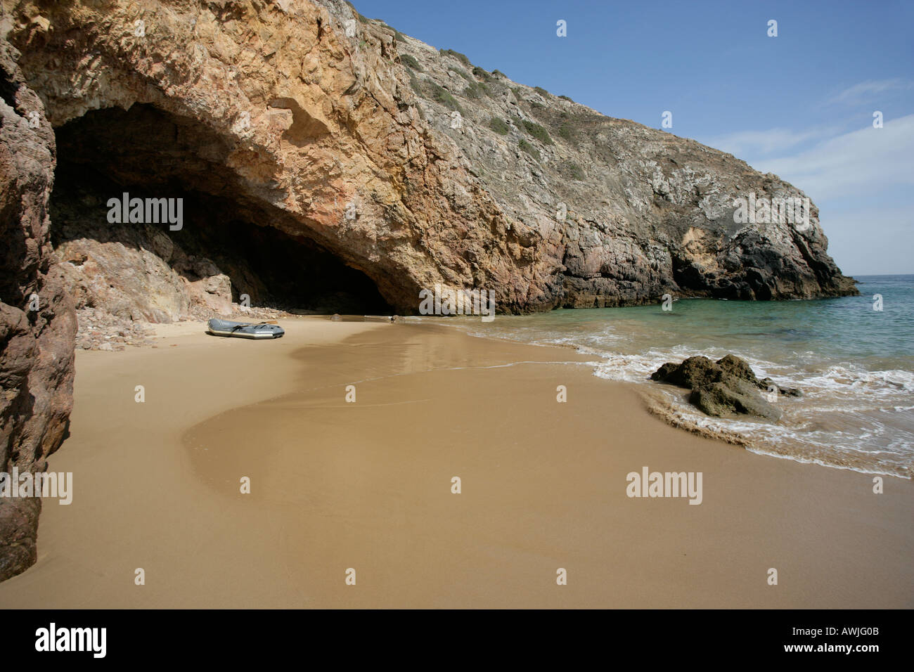 An inflatable dinghy pulled up onto secluded sandy beach next to a cave This beach is off Portugals Algarve coast Stock Photo