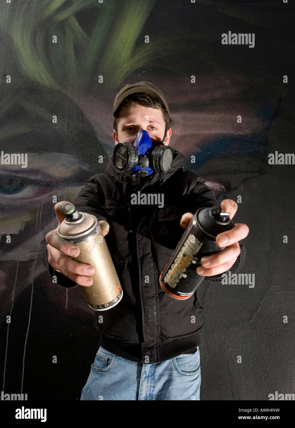 Graffiti Artist with mask spray paints a mural on a wall Stock Photo