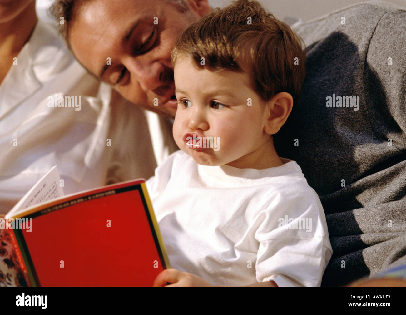 Young child making goofy face, looking at book with older man. Stock Photo