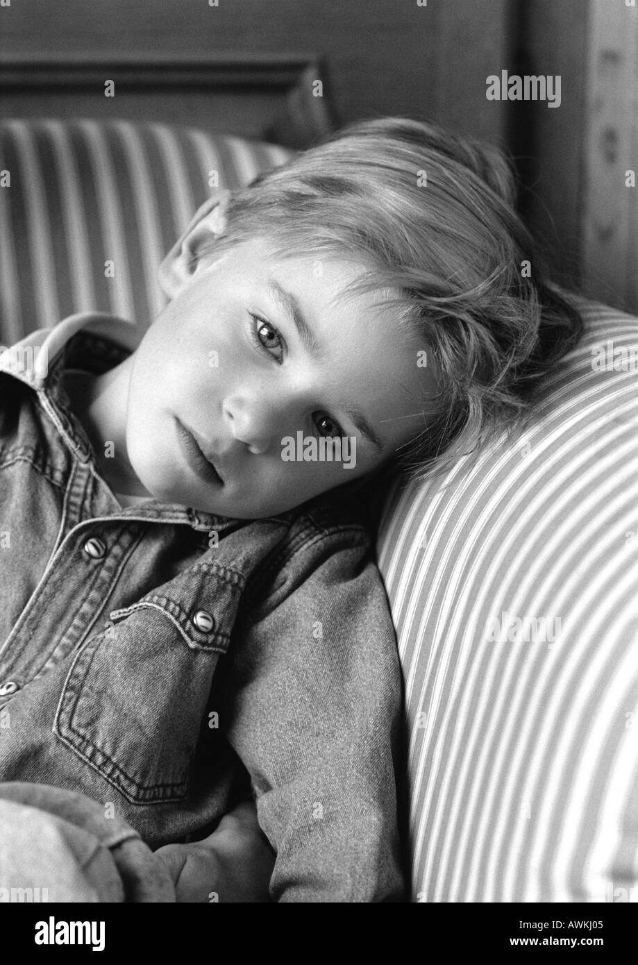 Young boy leaning head on chair arm, black and white portrait. Stock Photo