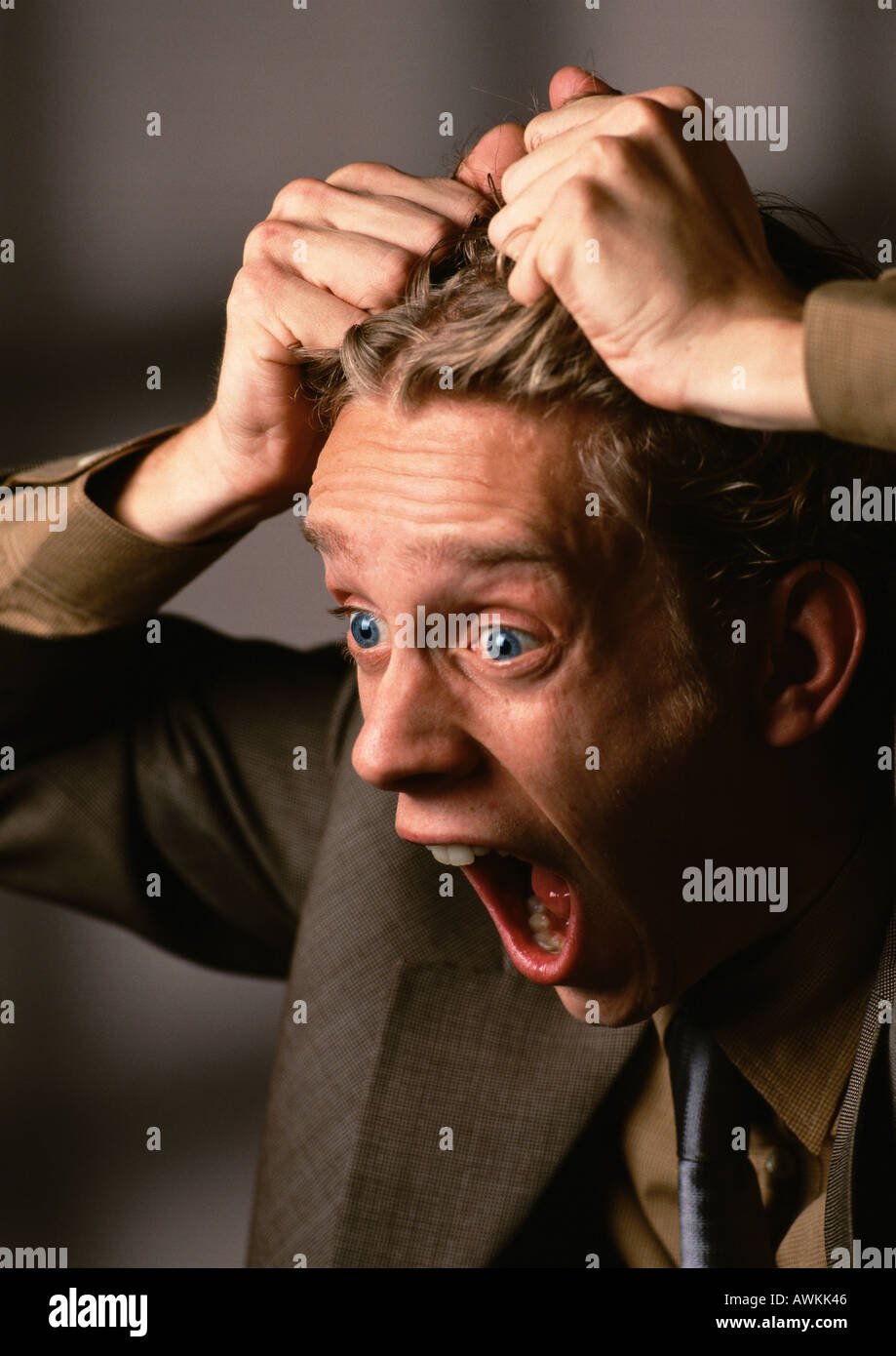 Man with mouth and eyes wide open, pulling hair, close-up Stock Photo
