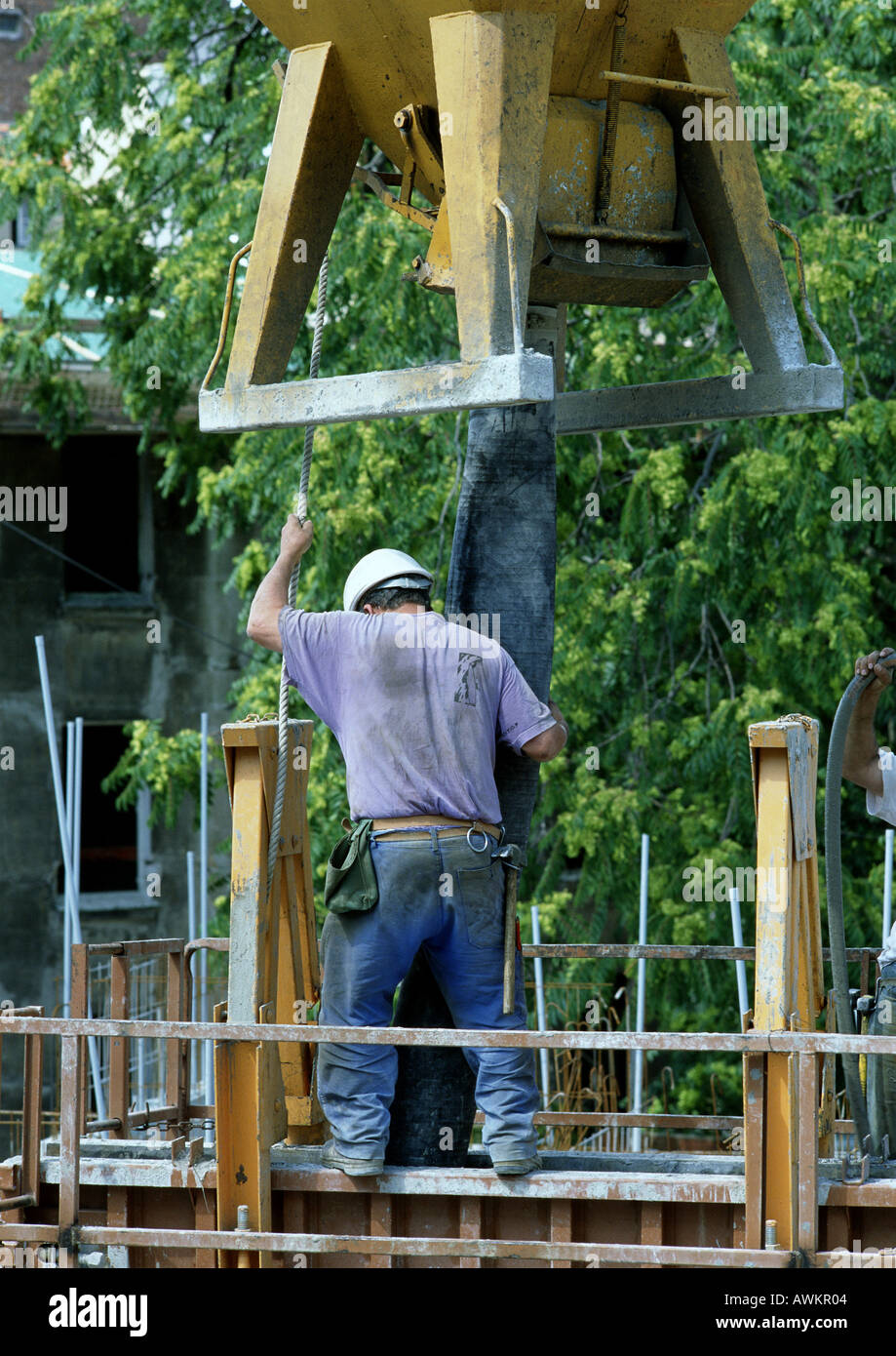 Construction worker holding pipe under cement mixer, rear view Stock Photo