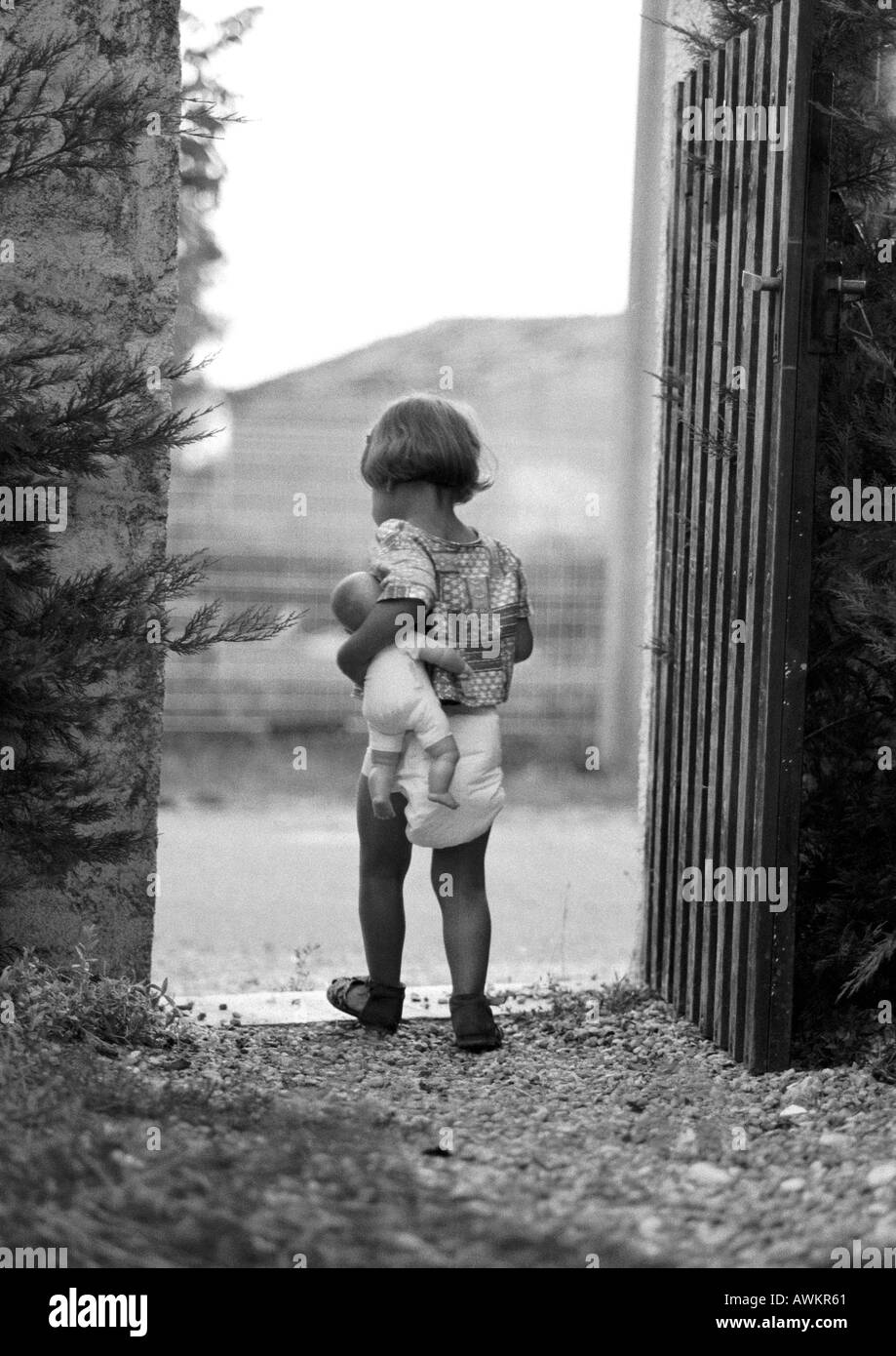 Little girl holding baby doll in gateway, rear view, b&w Stock Photo