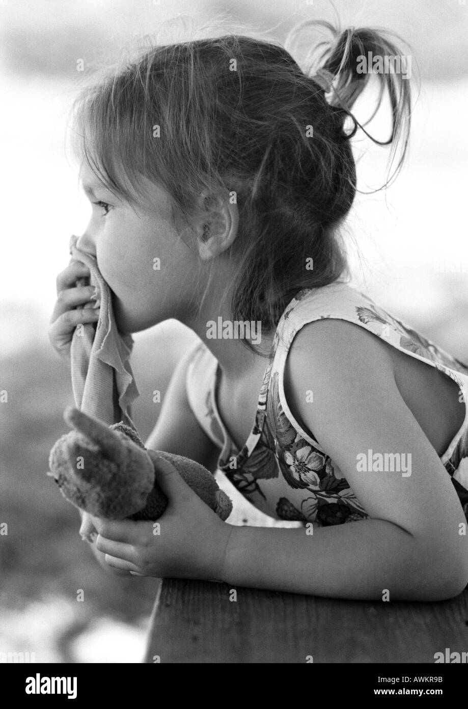 Girl holding stuffed animal in hand and piece of fabric over mouth, side view, b&w Stock Photo