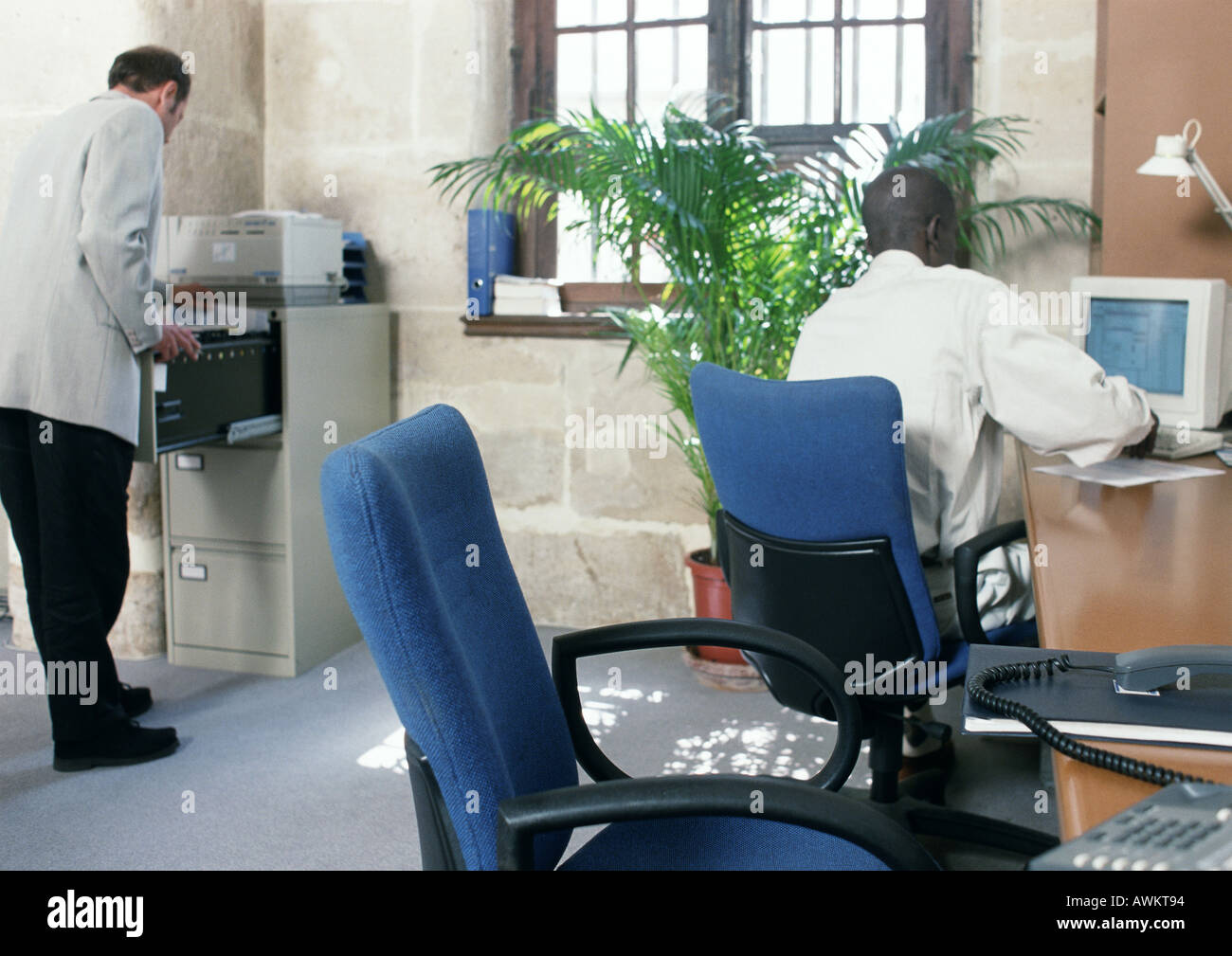 Two men in a room, one using computer, rear view Stock Photo - Alamy