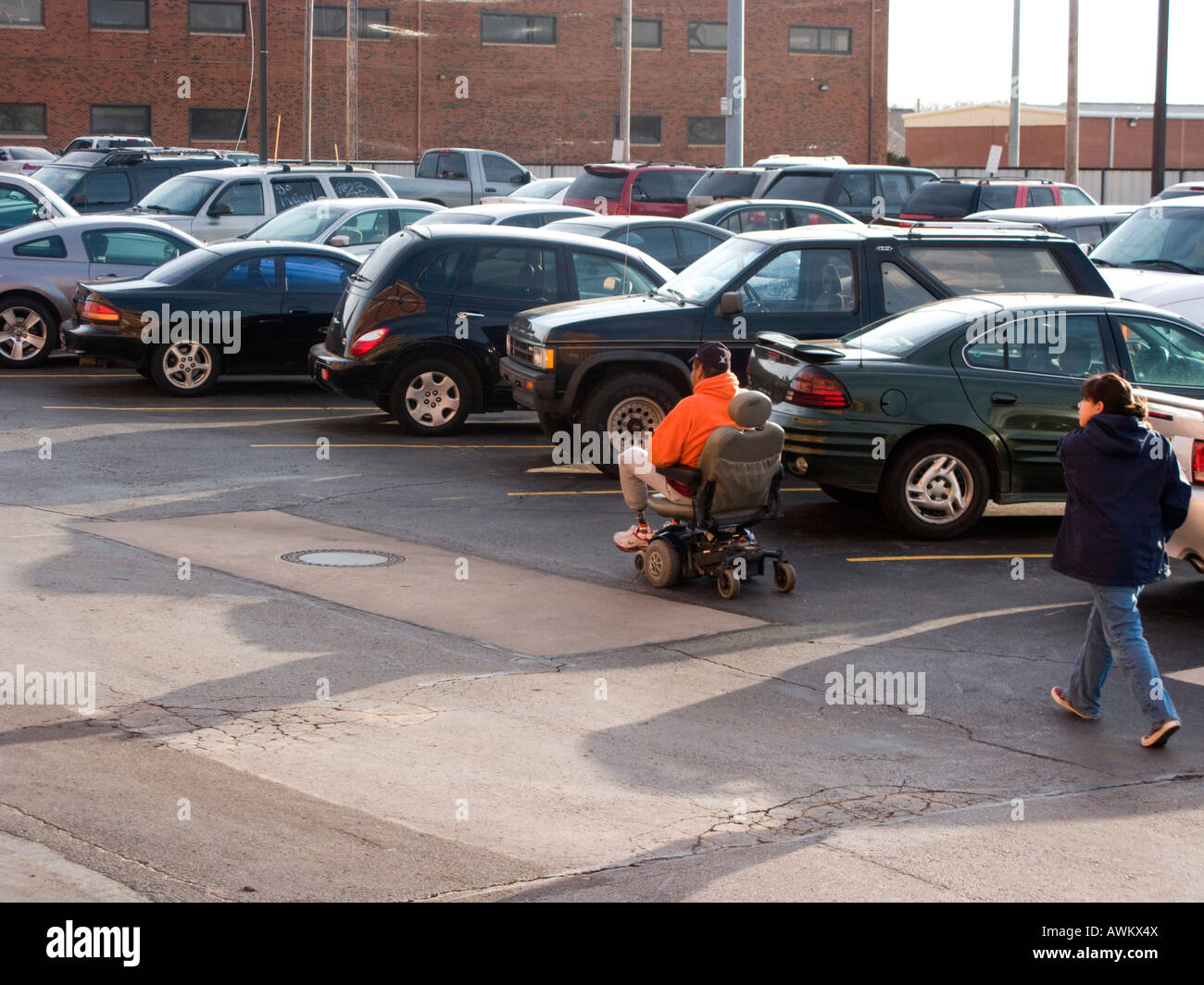 A handicapped man in a motorized wheelchair wheeling through a parking