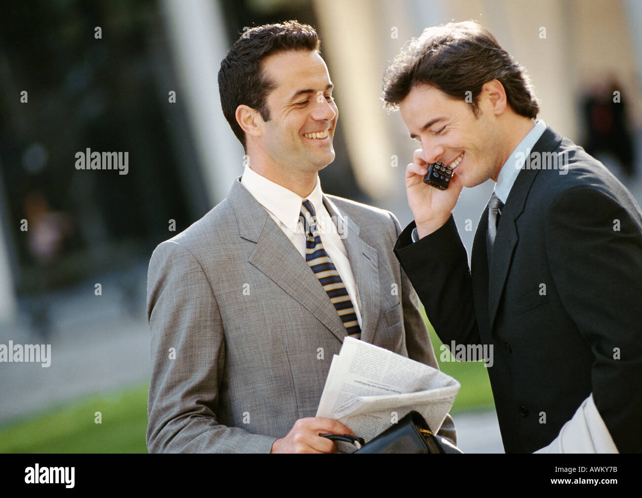 Two businessmen side by side outside, one using cell phone Stock Photo