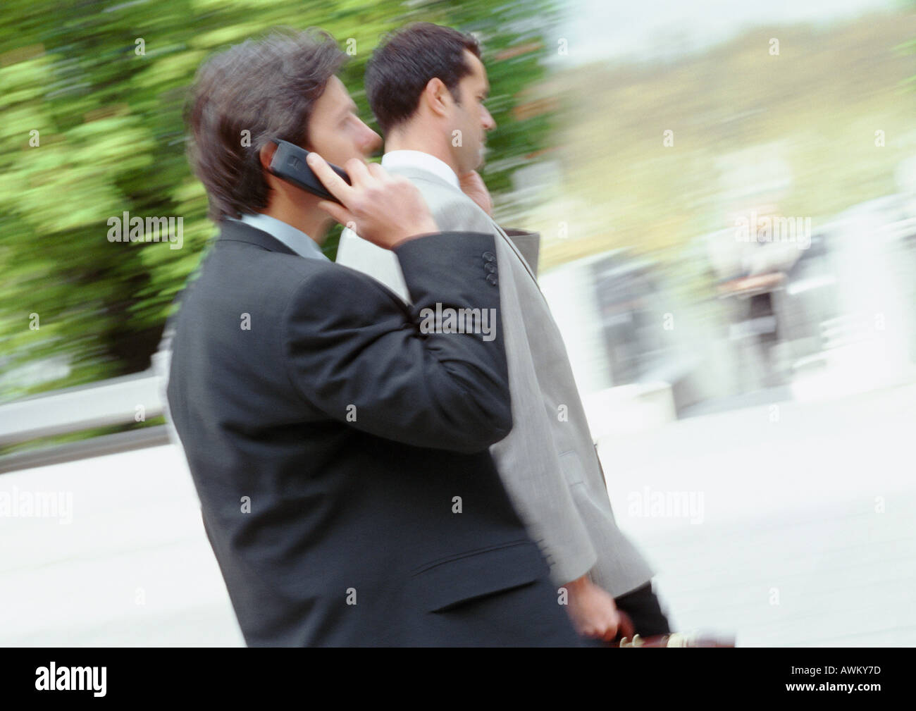 Two businessmen walking outside, using cell phones, side view Stock Photo