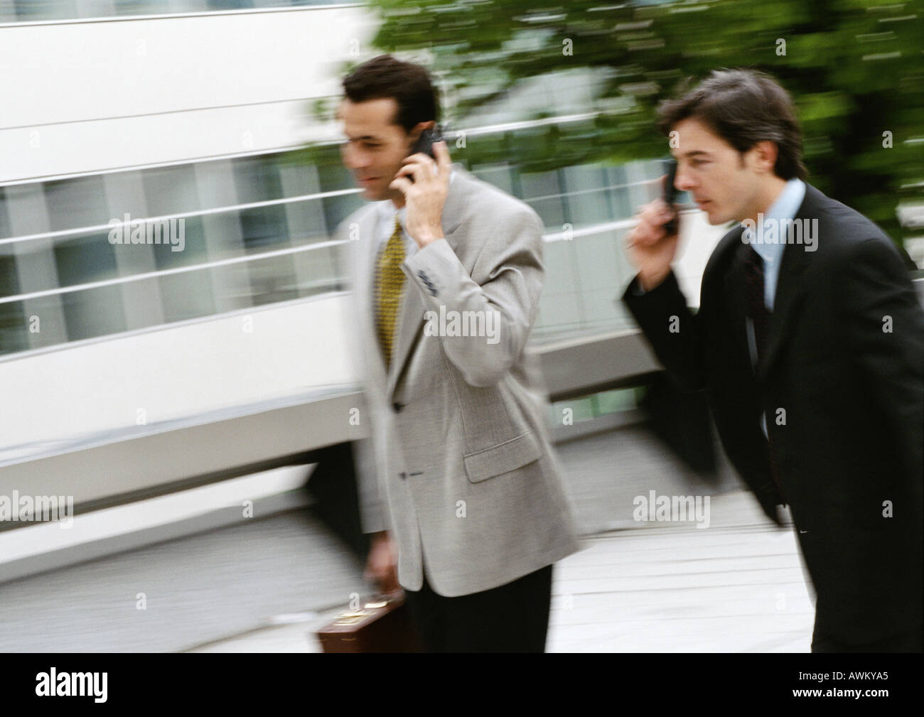 Two businessmen using cell phones outside, blurred Stock Photo