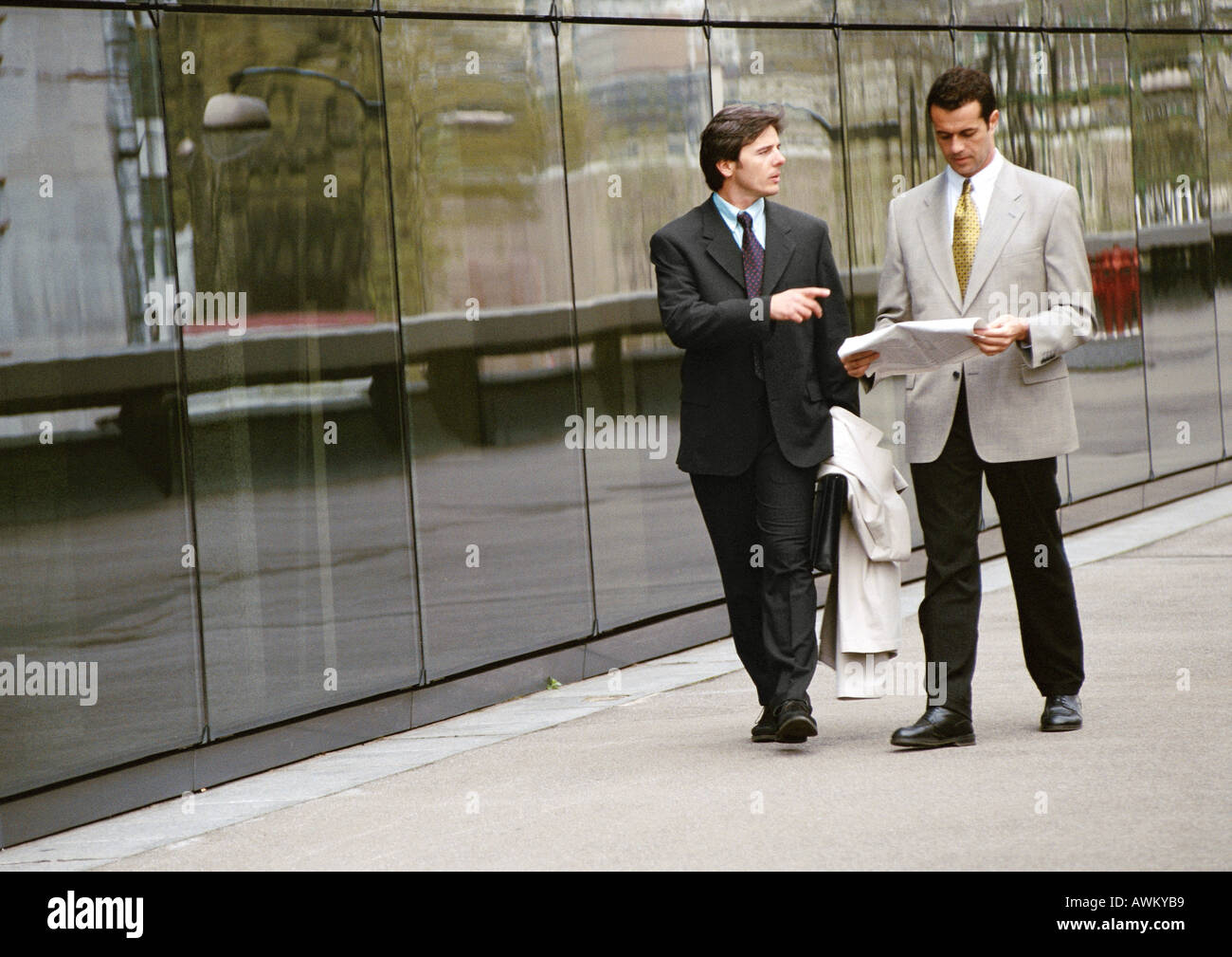 Two businessmen walking along sidewalk in front of building Stock Photo
