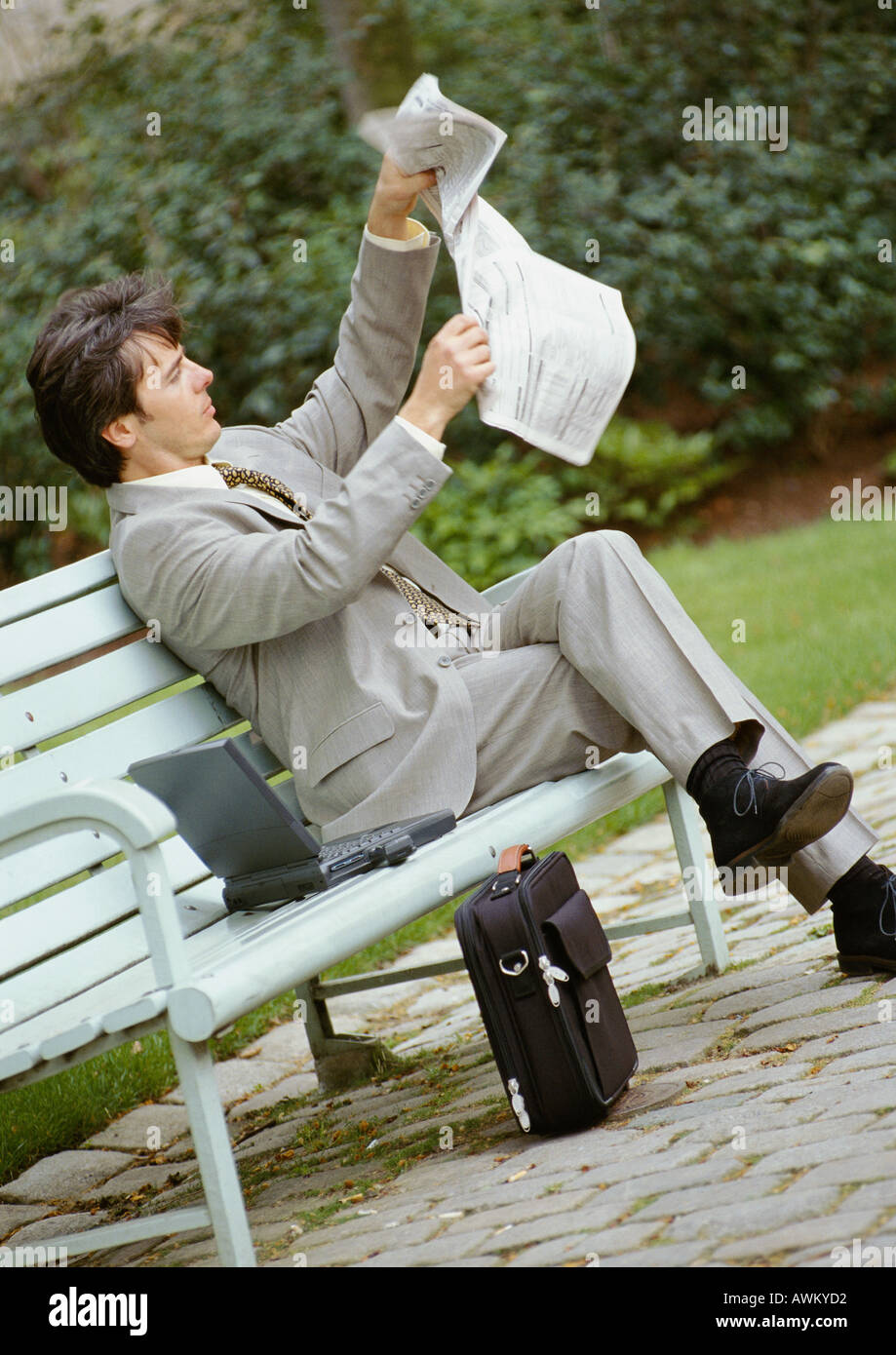 Businessman sitting on park bench, opening newspaper Stock Photo