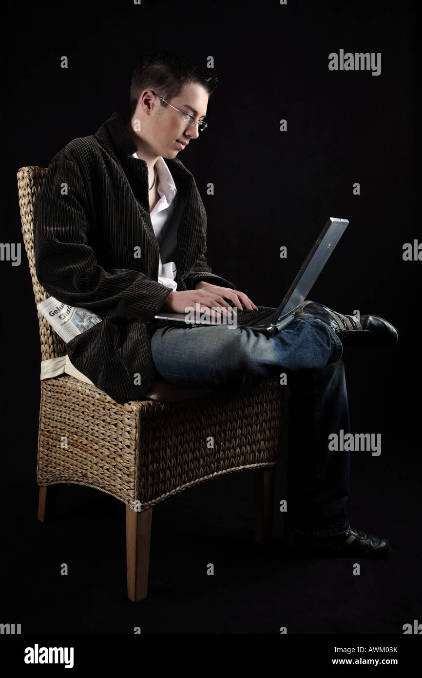 Young man sitting on a chair with a laptop on his lap Stock Photo