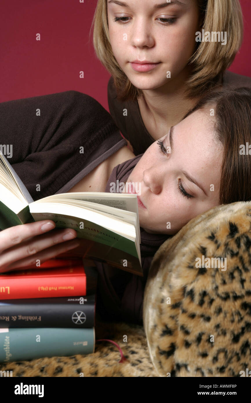 Two girls, pre-teens, early teens laying on a tiger-print sofa with a stack of schoolbooks Stock Photo