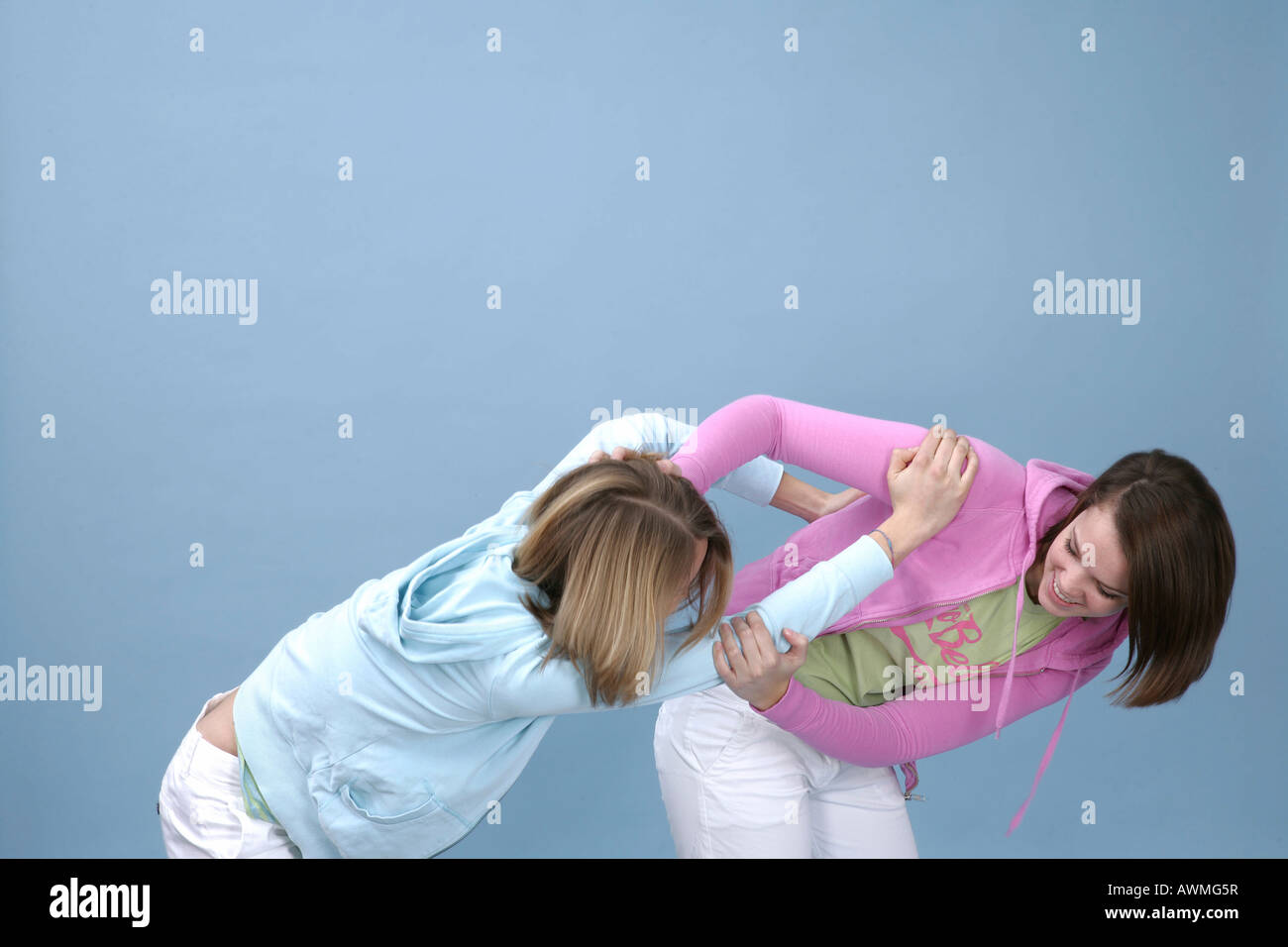 Two girls wearing casual outfits romping around in front of a light blue backdrop Stock Photo