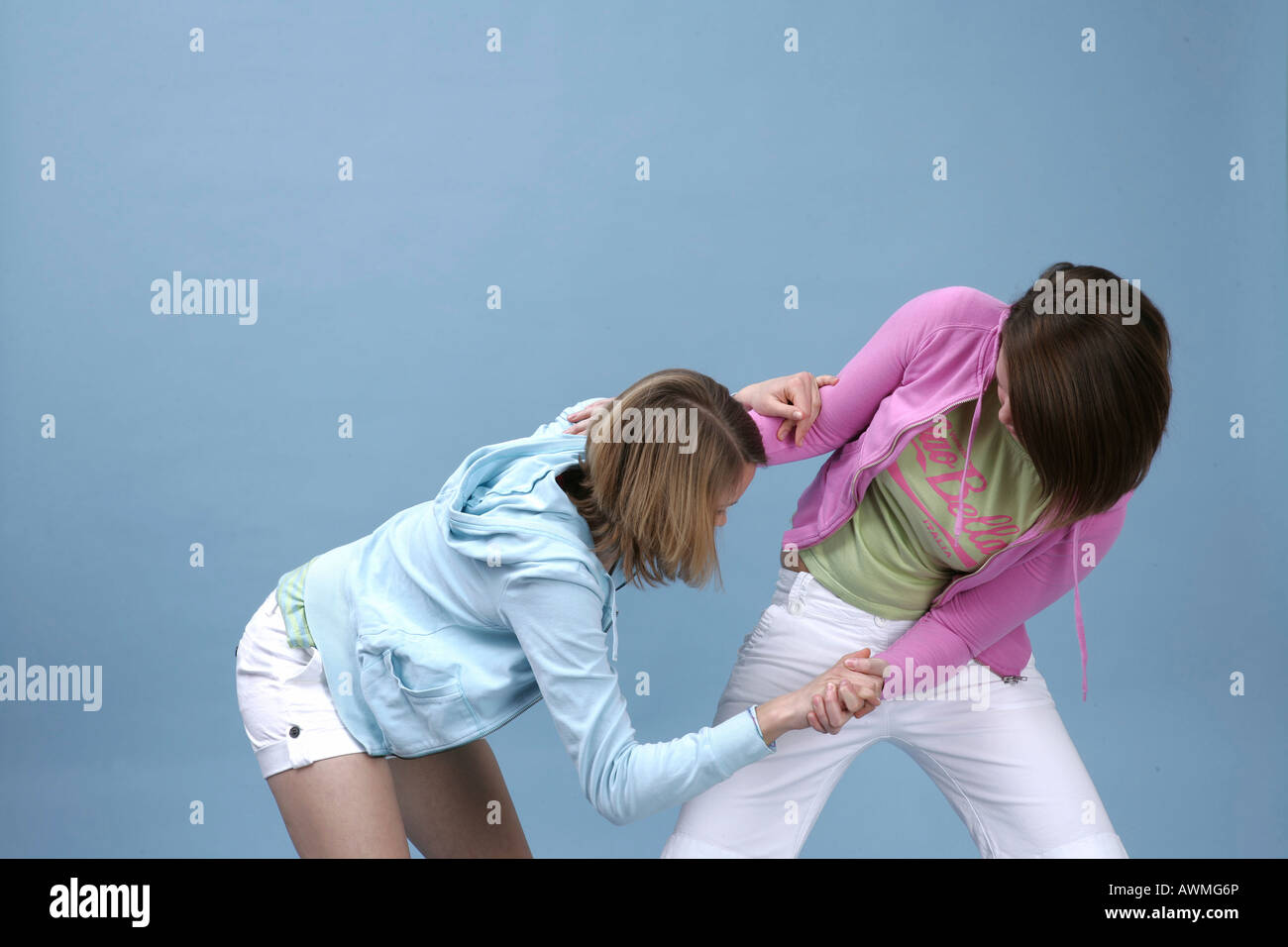Two girls wearing casual outfits romping around in front of a light blue backdrop Stock Photo