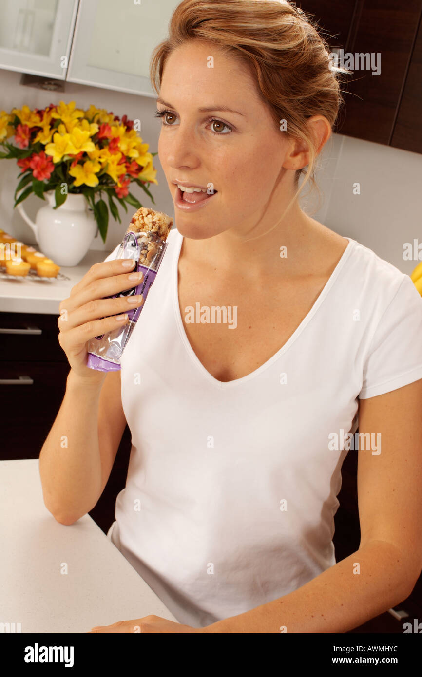 WOMAN IN KITCHEN EATING CEREAL BAR Stock Photo