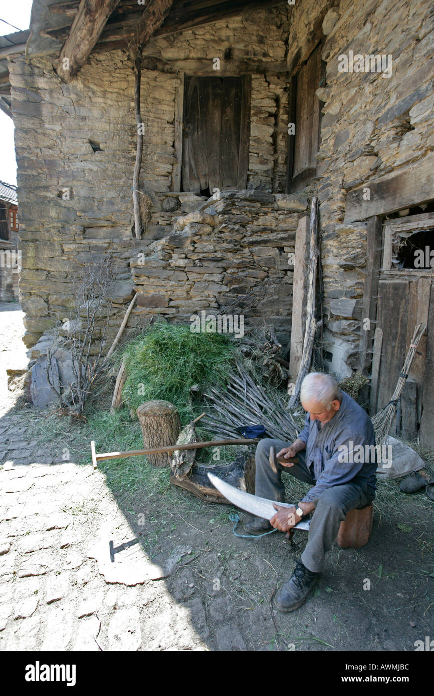A senior farmer sharpen the blade to a scythe in the Portuguese town of Rio de Onor Stock Photo