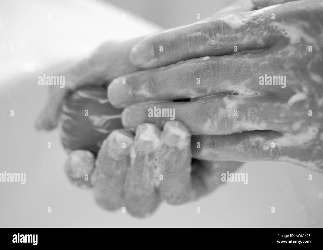 Hands covered with soap lather, holding bar of soap, closeup, b&w