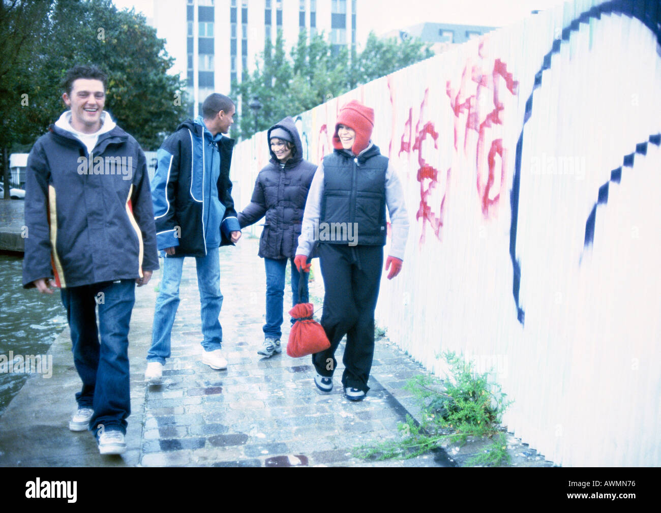 Four young people walking on sidewalk next to graffiti-covered wall Stock Photo
