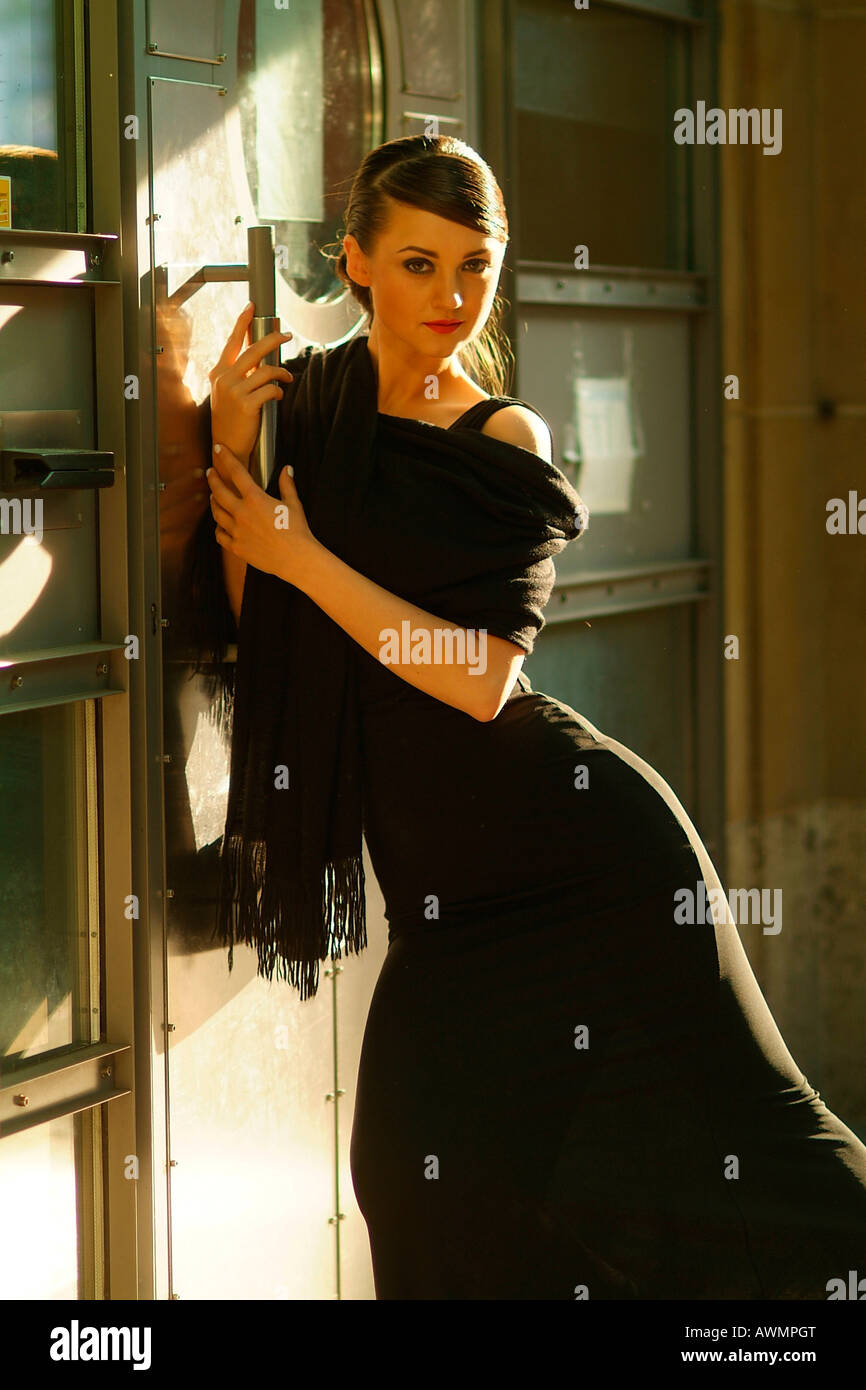 Young woman wearing black evening dress leaning against a door Stock Photo
