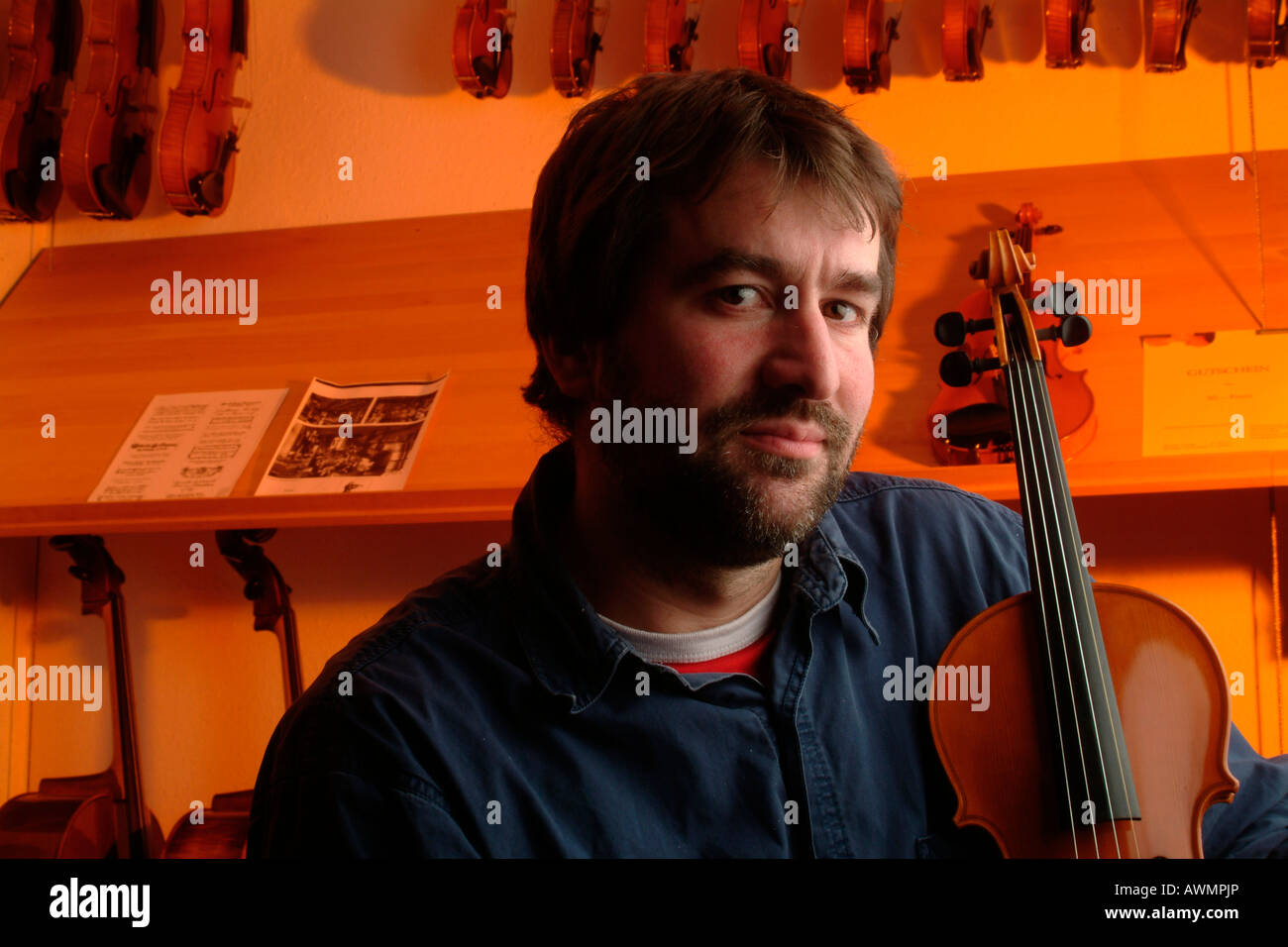 Violin-maker (luthier) in his showroom holding a violin Stock Photo