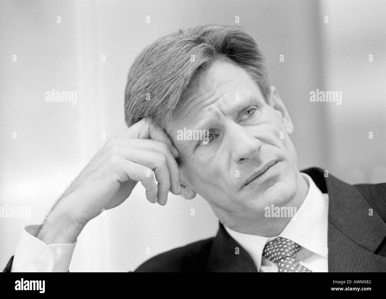 Businessman leaning head on hand and furrowing brow, close-up, black and white. Stock Photo