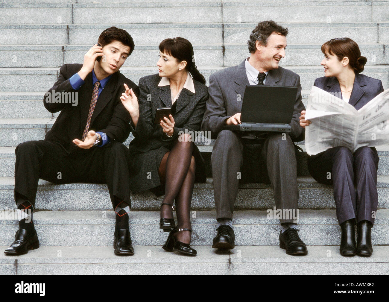 Four business people sitting on steps, interacting. Stock Photo