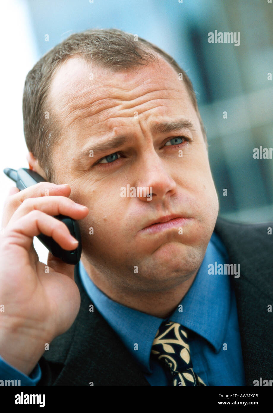 Businessman using cellular phone, puffing out cheeks and furrowing brow, portrait, close-up. Stock Photo