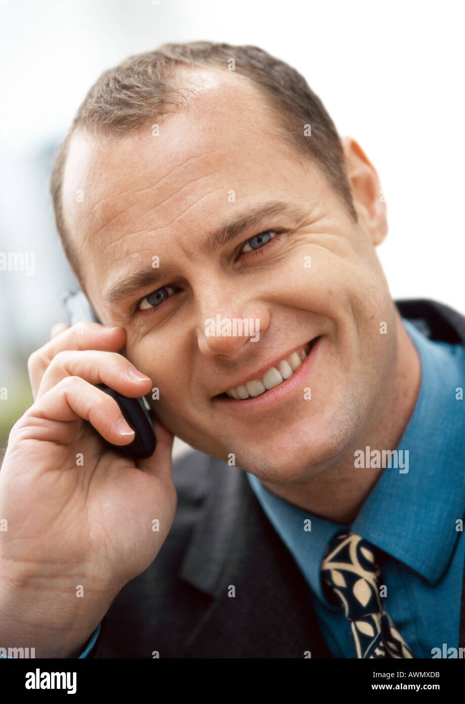Businessman using cellular phone, smiling at camera, portrait, close-up. Stock Photo
