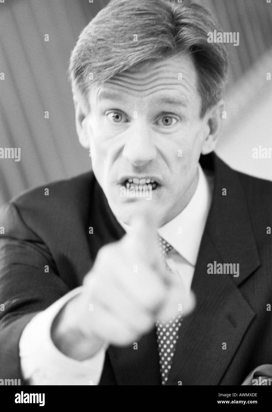 Businessman pointing at camera, hand blurred in foreground, black and white, portrait. Stock Photo