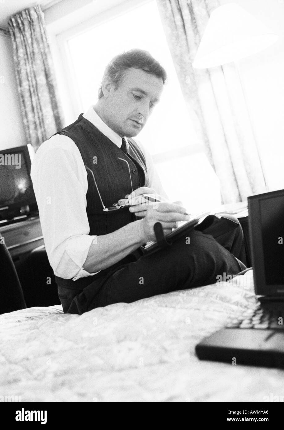 Businessman working, sitting on edge of bed in hotel room, blurred, b&w. Stock Photo