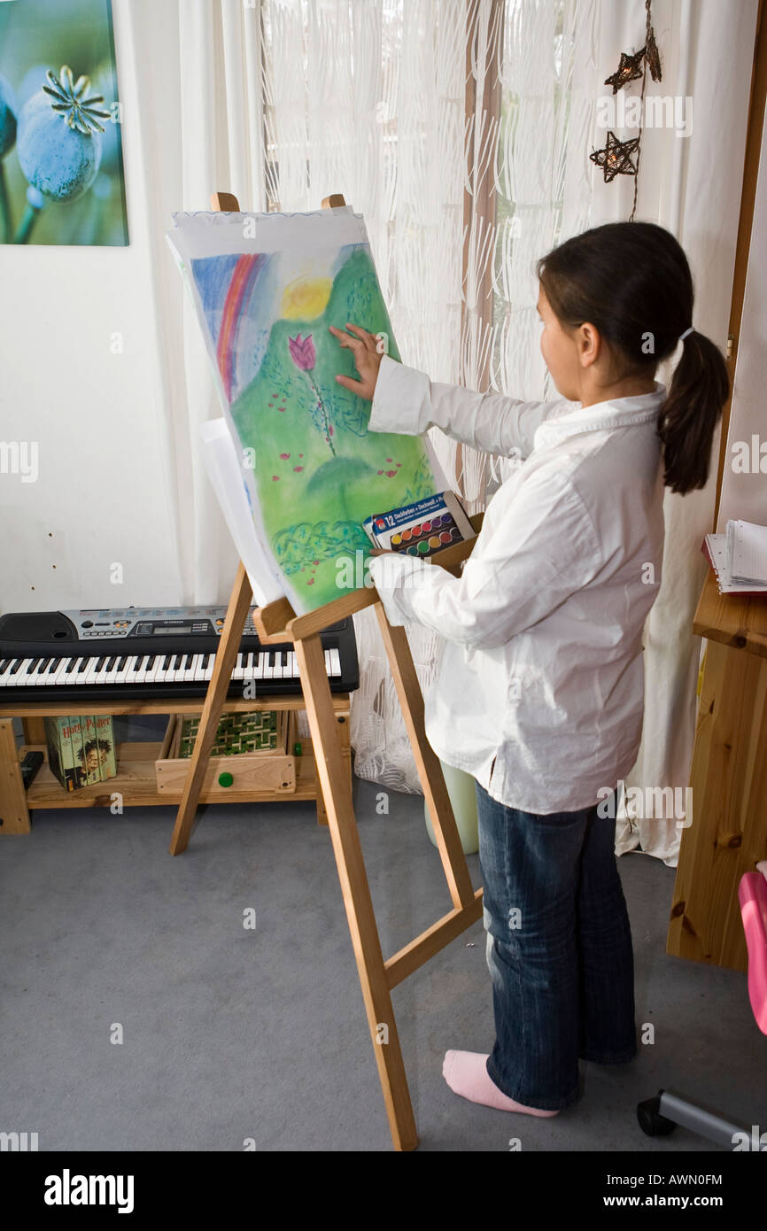 Young schoolgirl looking at painting, easel Stock Photo
