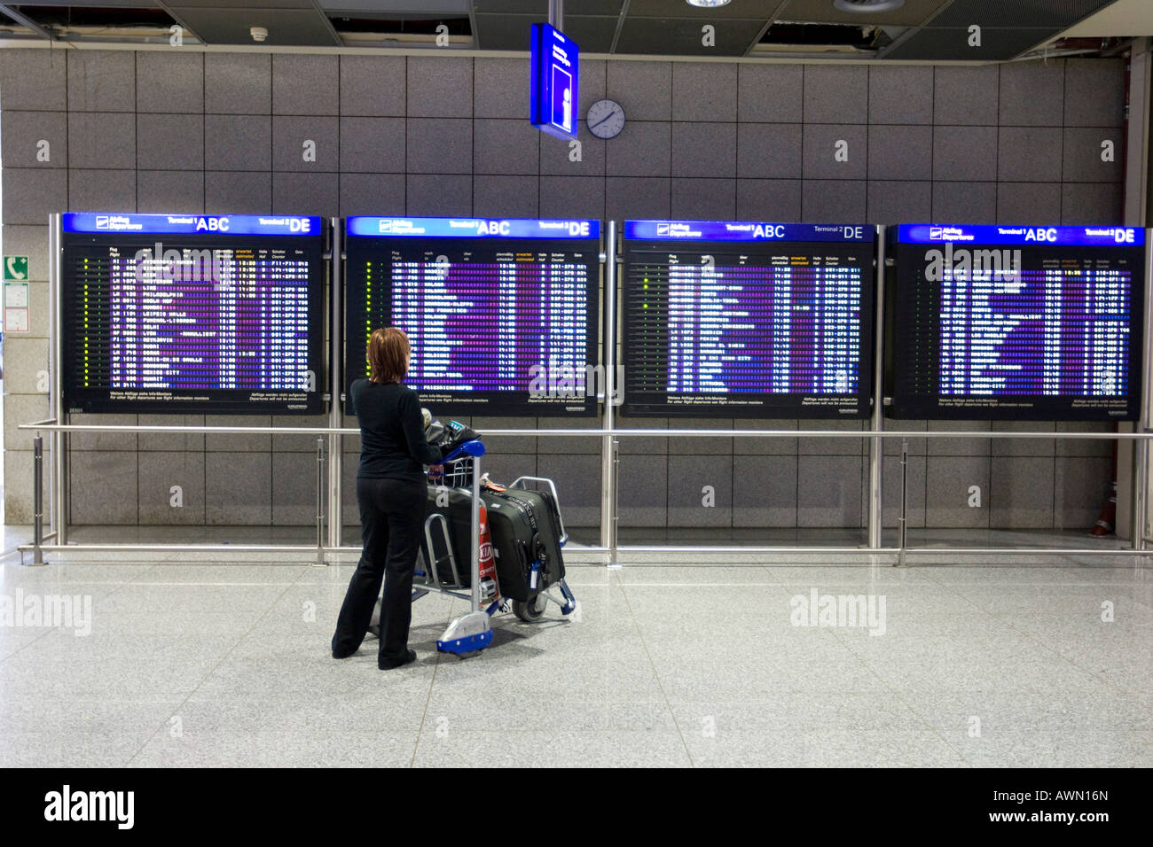 Passenger with luggage cart in front of flight info display screens
