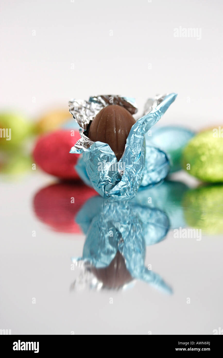 Chocolate Easter eggs laid out on a mirror, one partially unwrapped in the foreground Stock Photo