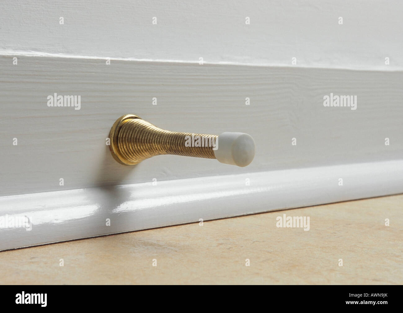 Brass spring door stop on white skirting board Stock Photo Alamy