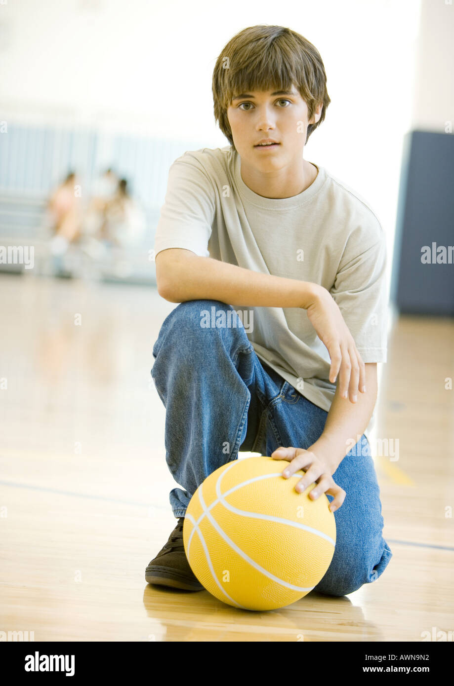 Teen boy crouching with basketball in school gym Stock Photo