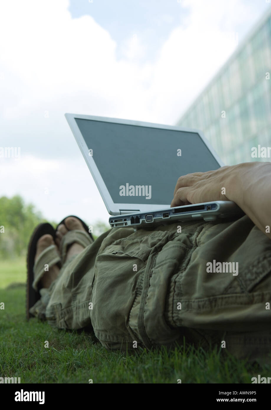 Man lounging in grass, using laptop Stock Photo
